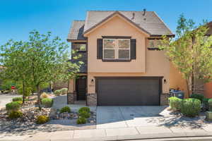 View of front facade with stone siding, a garage, concrete driveway, and stucco siding