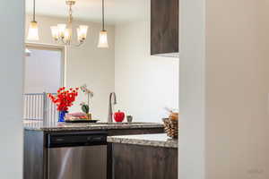 Kitchen featuring dark wood finish cabinets, stainless steel dishwasher, light stone counters, and a chandelier