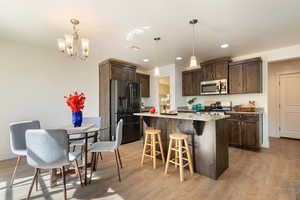 Kitchen featuring dark wood finish cabinets, a breakfast bar, stainless steel appliances, light stone counters, and light wood-style flooring