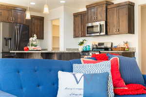 Kitchen featuring dark wood finish cabinets, stainless steel appliances, decorative light fixtures, a kitchen island, and a breakfast bar area