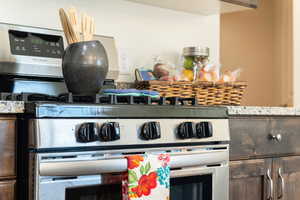 Kitchen view of stainless steel gas range oven, stone countertops, and dark wood finish cabinetry