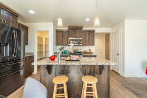 Kitchen featuring dark wood finish cabinets, stainless steel appliances, light stone counters, and hanging light fixtures