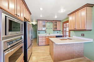 Kitchen with glass fronted cabinets, stainless steel appliances, light countertops, a peninsula, and light wood-style flooring