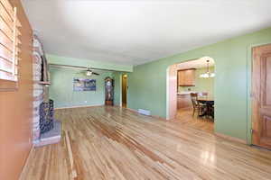 Unfurnished living room featuring arched walkways, light wood-style flooring, a brick fireplace, and a ceiling fan