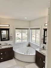 Bathroom featuring two vanities, a whirlpool tub, and tile walls