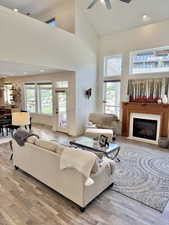 Living area featuring recessed lighting, a high ceiling, light wood-style flooring, a glass covered fireplace, and ceiling fan