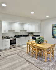 Kitchen with stainless steel range with gas stovetop, white cabinetry, dark countertops, light wood finished floors, and recessed lighting