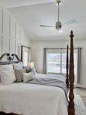 Bedroom featuring lofted ceiling, light wood-type flooring, multiple windows, a ceiling fan, and a decorative wall
