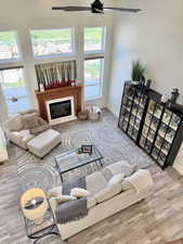 Living room with light wood-style flooring, ceiling fan, a glass covered fireplace, plenty of natural light, and a high ceiling