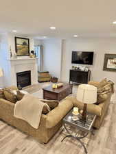 Living room with light wood-type flooring, a glass covered fireplace, and recessed lighting