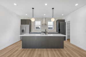 Photos of a finished unit - Kitchen featuring dark wood finish cabinets, stainless steel fridge, light wood finished floors, decorative light fixtures, and a center island with sink