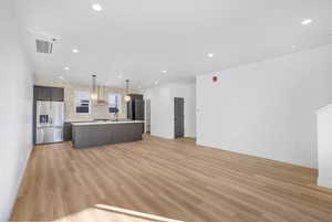 Photos of a finished unit - Kitchen featuring open floor plan, light countertops, dark wood finish cabinets, stainless steel fridge, and an island with sink