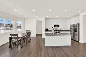 Kitchen with stainless steel appliances, dark stone countertops, white cabinetry, a kitchen island with sink, and recessed lighting
