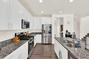 Kitchen featuring stainless steel appliances, white cabinets, dark stone countertops, dark wood finished floors, and recessed lighting