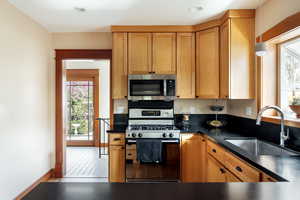 Kitchen with gas stove, dark countertops, stainless steel microwave, wood finish cabinets, and plenty of natural light