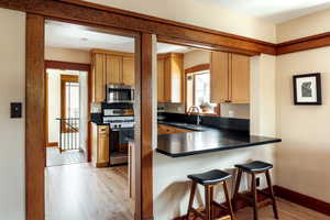 Kitchen featuring a kitchen breakfast bar, stainless steel appliances, light wood-style flooring, a peninsula, and dark countertops