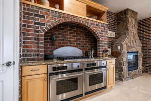Kitchen with double oven, open shelves, dark stone countertops, a multi sided fireplace, and light wood finish cabinets