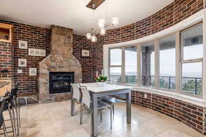 Dining room featuring brick wall, a chandelier, a stone fireplace, and light tile patterned flooring