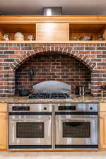 Kitchen with open shelves, light stone counters, light wood finish cabinetry, and stainless steel double oven