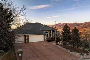 French country inspired facade featuring an attached garage, concrete driveway, brick siding, roof with shingles, and a mountain view