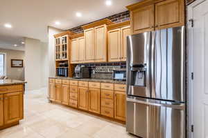 Kitchen featuring stainless steel fridge with ice dispenser, recessed lighting, dark stone counters, glass insert cabinets, and black microwave