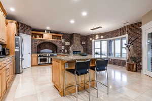 Kitchen featuring light stone counters, a kitchen island with sink, a kitchen breakfast bar, stainless steel appliances, and light wood finish cabinets