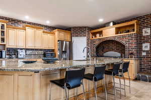 Kitchen featuring open shelves, brick wall, light wood finish cabinets, light stone countertops, and stainless steel appliances