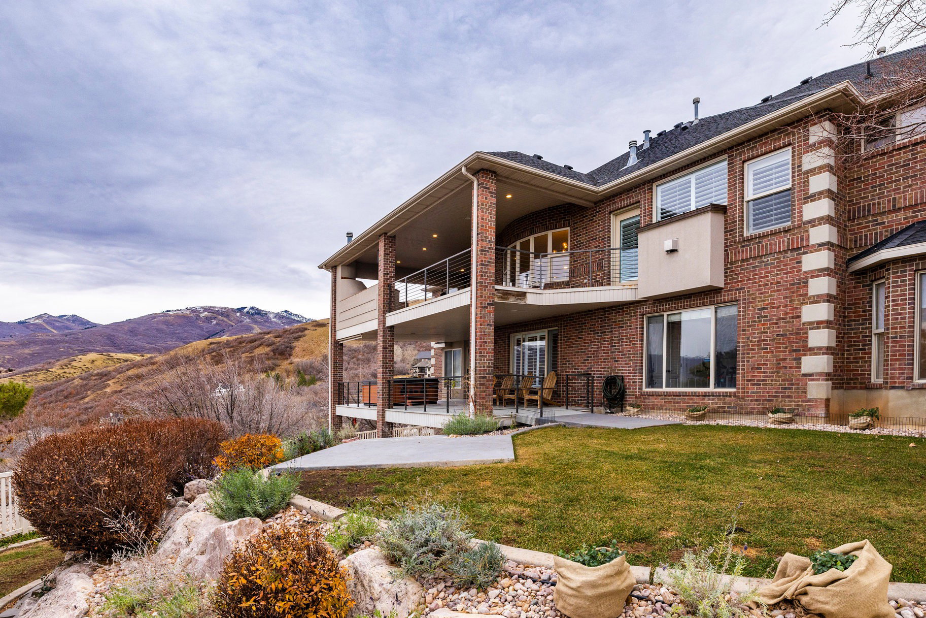 Rear view of property featuring a patio, brick siding, a balcony, a mountain view, and a yard