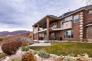 Rear view of property featuring a patio, brick siding, a balcony, a mountain view, and a yard