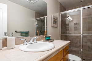 Full bath with vanity, a shower stall, and a textured ceiling