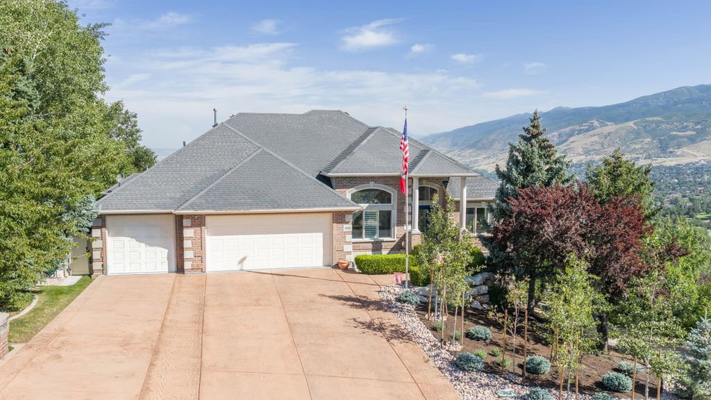 Brick and stucco facade with an attached three-car garage, dark shingle roofing, and a concrete driveway