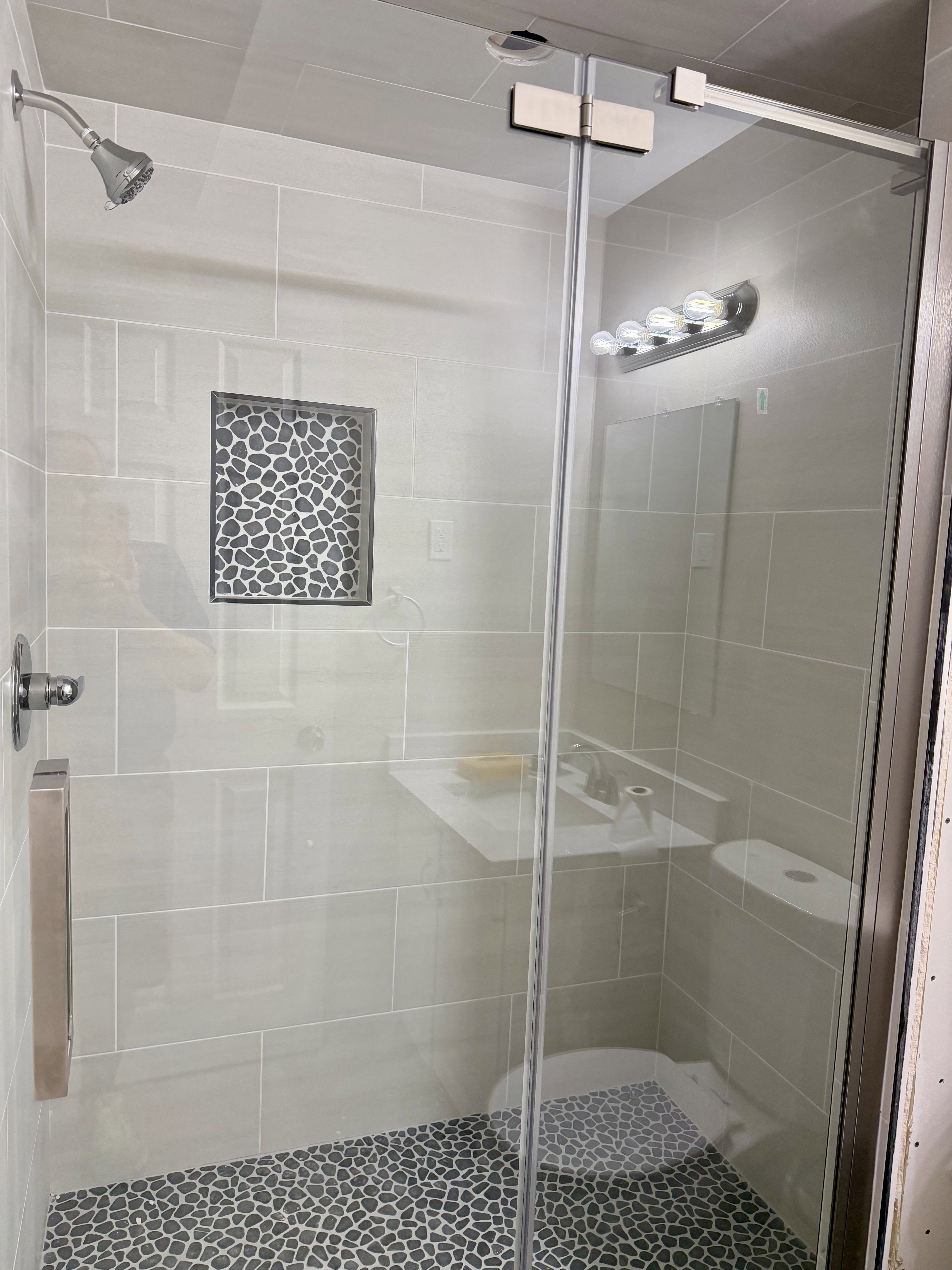 Glass-enclosed shower featuring a pebble-stone floor and a tile niche with decorative stone inlay