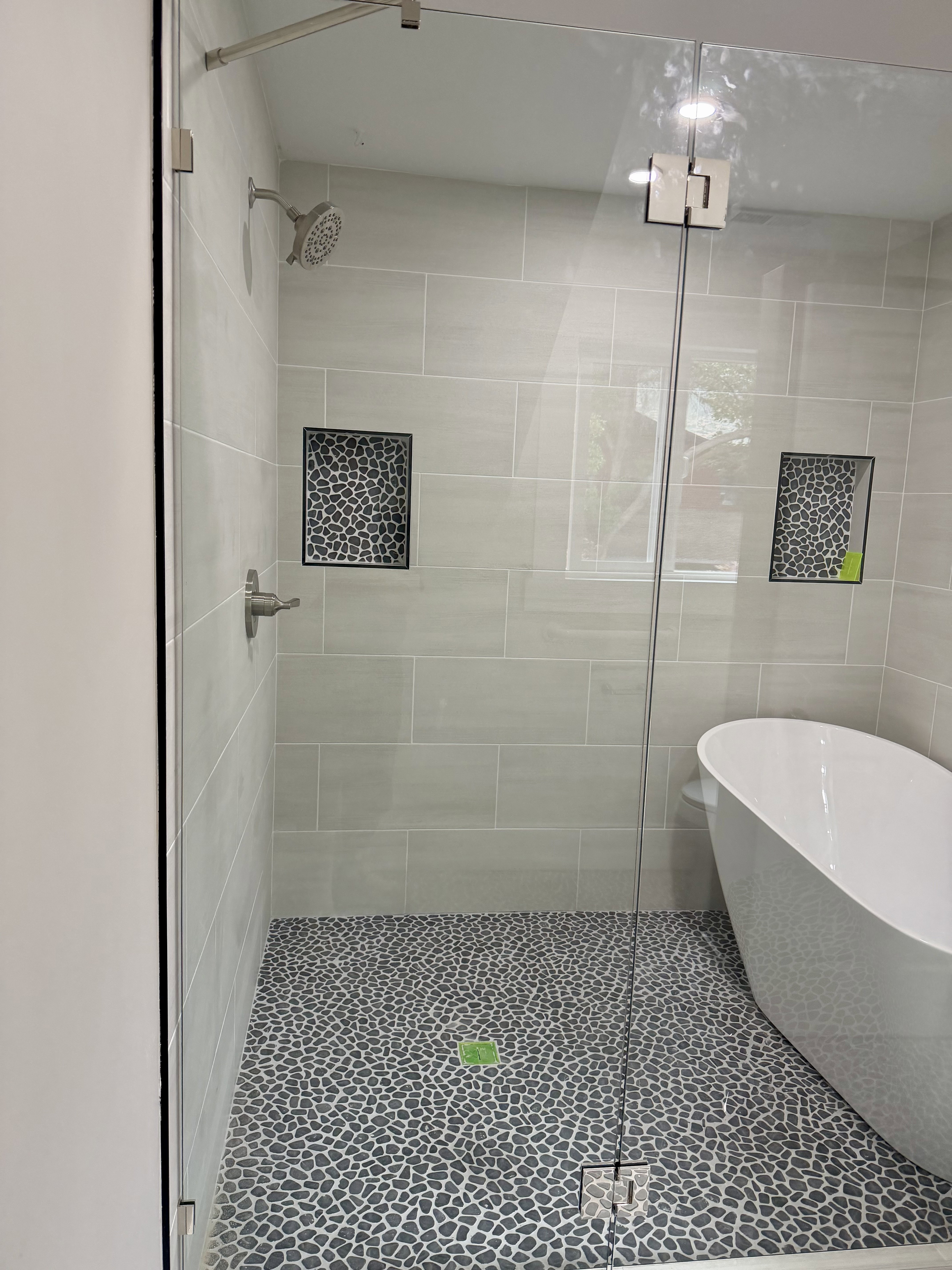 Glass-enclosed shower featuring a pebble-stone floor, light-toned rectangular wall tiles, and built-in shower niches