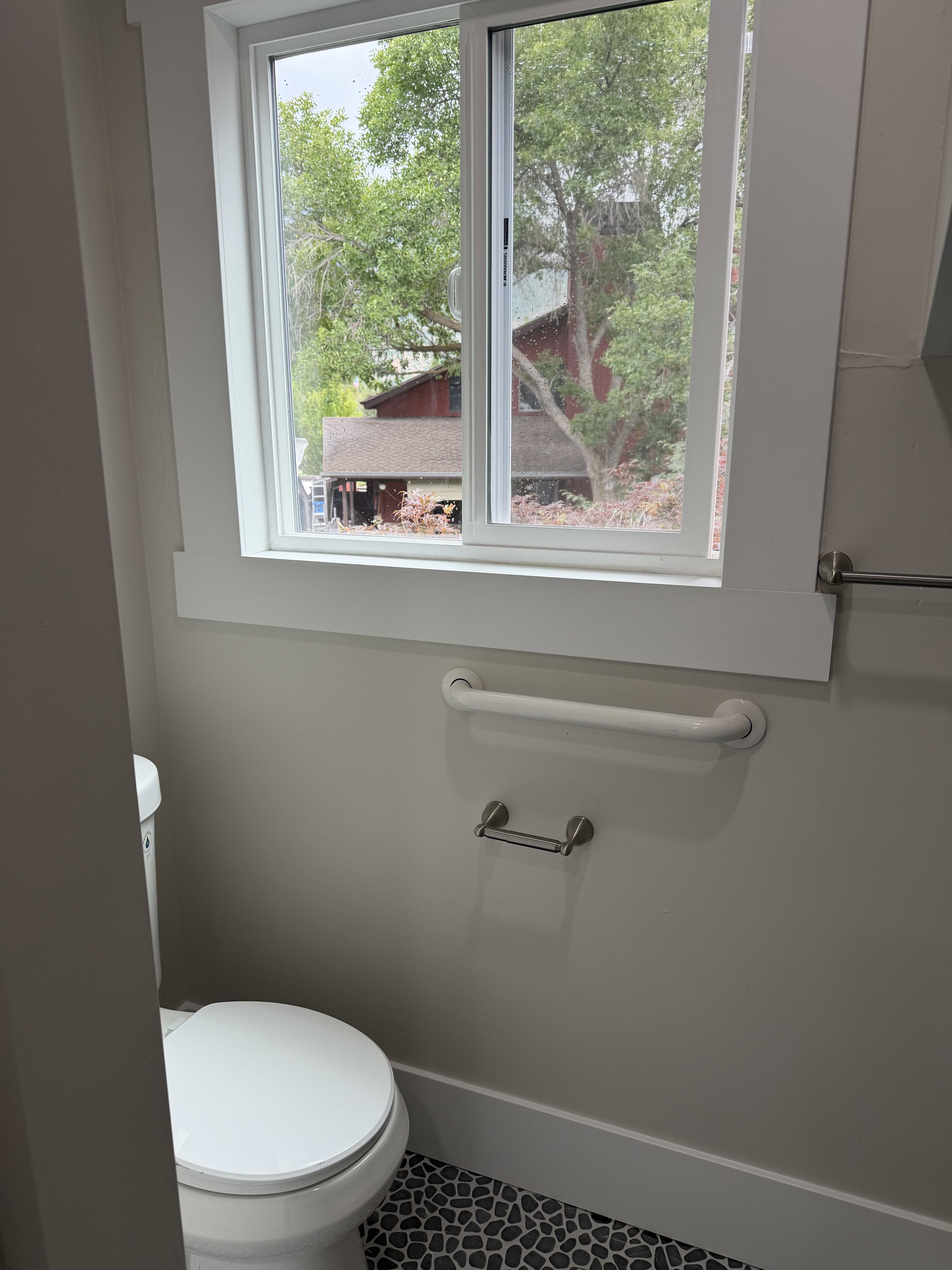 Bathroom featuring a white toilet, pebble-style flooring, a sliding window with white trim, a towel bar, and a grab bar