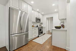Kitchen featuring white cabinets, stainless steel appliances, light wood-style flooring, recessed lighting, and tasteful backsplash