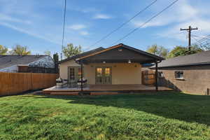 Rear view of house with stucco siding, a fenced backyard, a wooden deck, and french doors