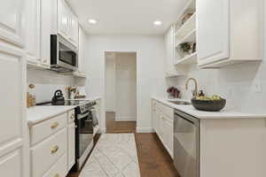 Kitchen with stainless steel appliances, white cabinets, open shelves, dark wood-style flooring, and recessed lighting