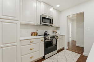 Kitchen featuring stainless steel appliances, white cabinets, dark wood-type flooring, tasteful backsplash, and recessed lighting