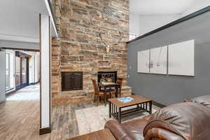 Living area with a stone fireplace, wood finished floors, and a high ceiling