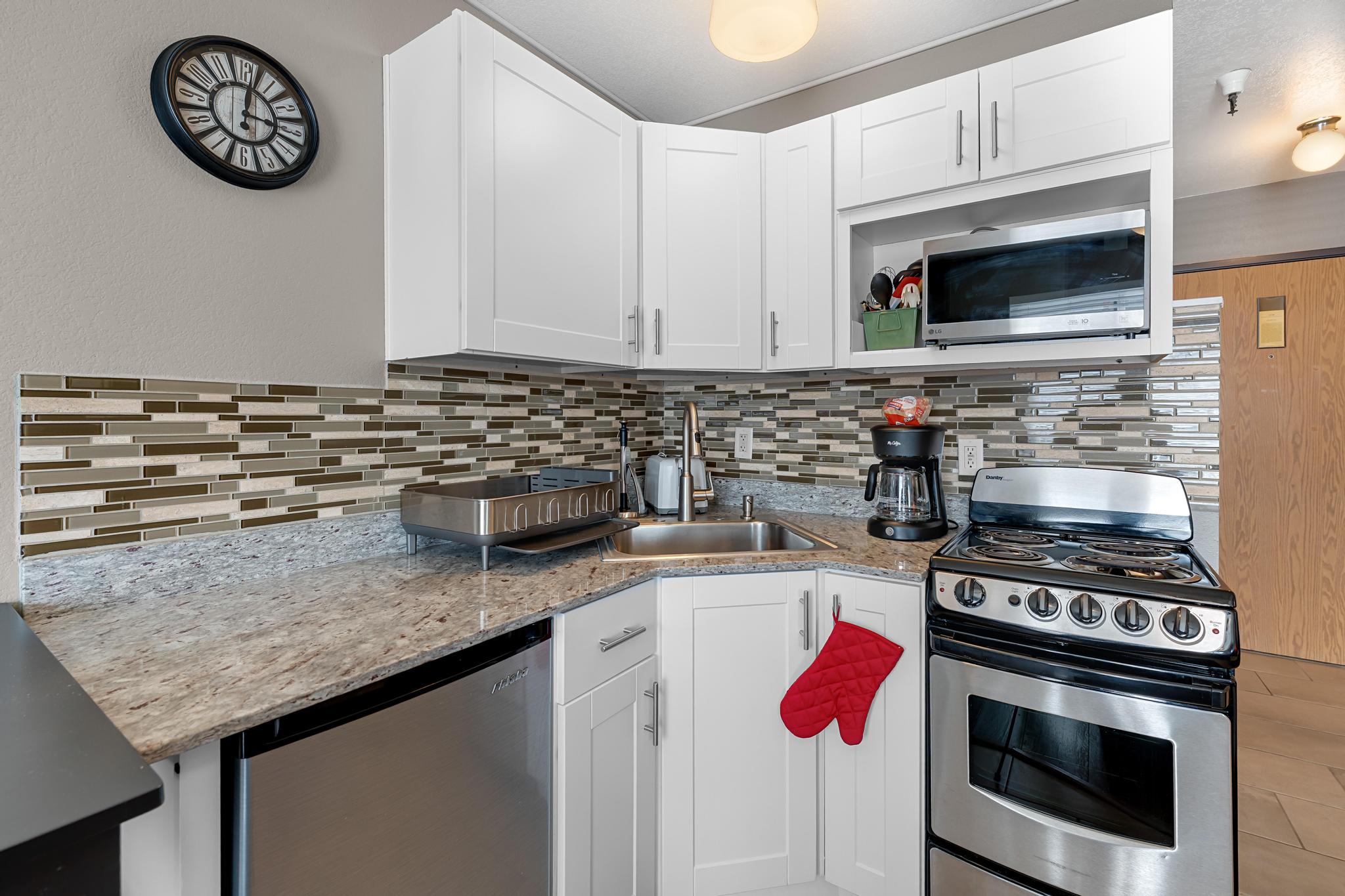 Kitchen with stainless steel appliances, light stone counters, white cabinetry, and tasteful backsplash