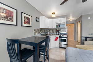 Kitchen featuring stainless steel appliances, a ceiling fan, white cabinets, and tasteful backsplash