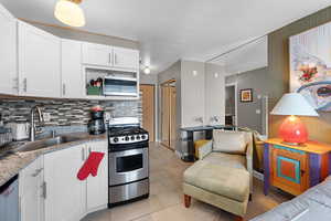 Kitchen with stainless steel appliances, white cabinets, light stone countertops, light tile patterned flooring, and backsplash