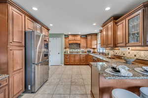Kitchen featuring wood finish cabinets, stainless steel appliances, light stone countertops, decorative backsplash, and recessed lighting