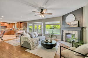 Living area with light wood-style floors, a glass covered fireplace, a textured ceiling, french doors, and ceiling fan