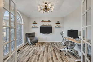 Office space with light wood-style flooring, french doors, hanging lights, and a raised ceiling
