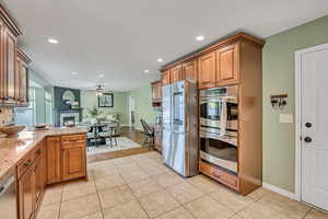 Kitchen with wood finish cabinetry, stainless steel appliances, light stone counters, open floor plan, and a fireplace