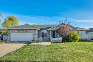 Single story home featuring an attached garage, roof with shingles, concrete driveway, brick siding, and a front lawn