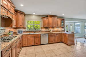 Kitchen with a peninsula, wood finish cabinets, a kitchen bar, stainless steel appliances, and light stone counters