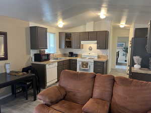 Kitchen with light countertops, white appliances, light LVT flooring, and brown cabinetry, vaulted ceilings.