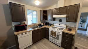 Kitchen with white appliances, light countertops, light LVT  floors, vaulted ceiling, and dark wood finish cabinetry